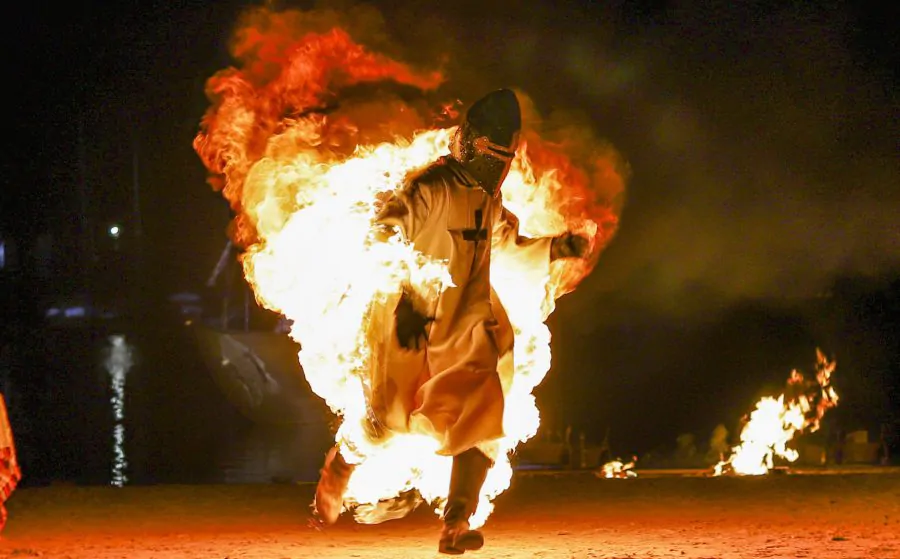 Actor medieval envuelto en llamas durante una impactante escena de fuego en una recreación histórica nocturna