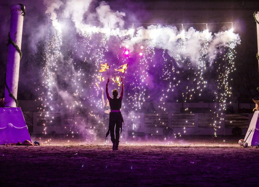 Artista sosteniendo antorchas en una presentación nocturna con fuegos artificiales y efectos de luces en un escenario