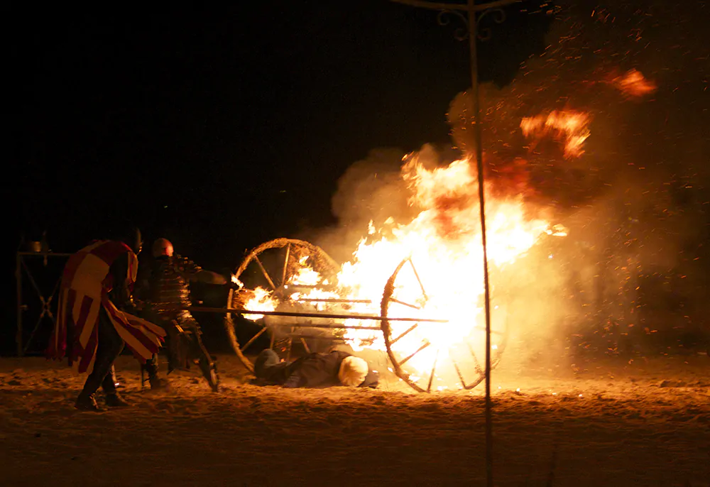 Explosión de una carreta en llamas durante una recreación medieval nocturna con guerreros en plena batalla