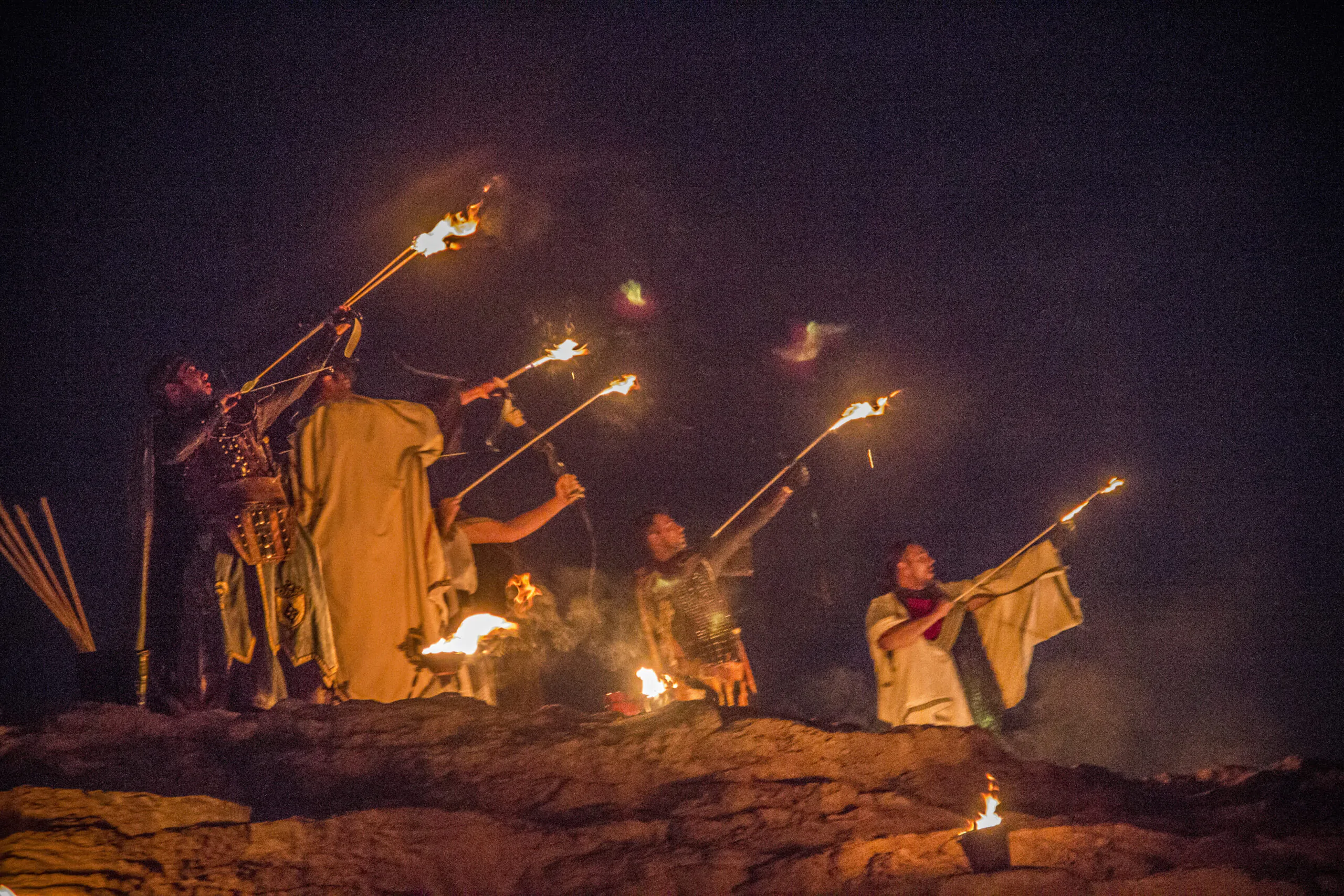 Guerreros medievales encendiendo flechas con fuego durante una representación nocturna en un evento histórico