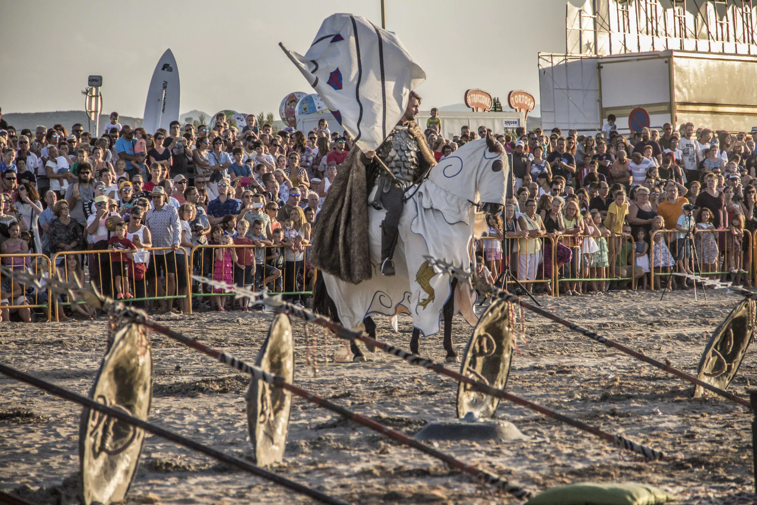 Caballero medieval participando en una justa a caballo, ondeando una bandera frente a una multitud