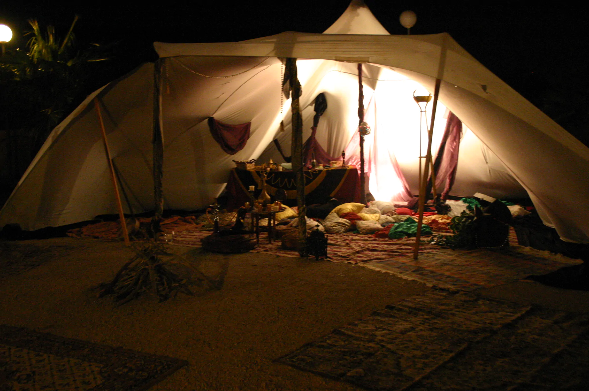 Tienda iluminada en la noche con decoración interior de cojines y alfombras, ambientada para un evento o reunión temática