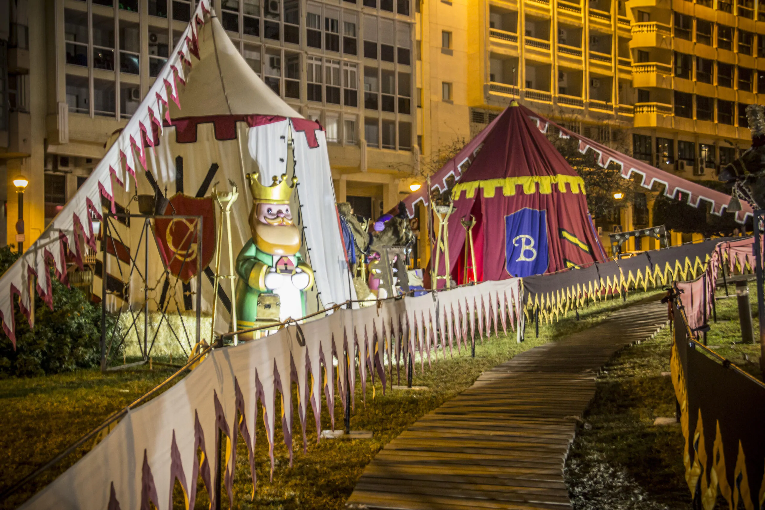 Campamento medieval iluminado con tiendas decoradas y una figura de rey, en una exhibición nocturna temática