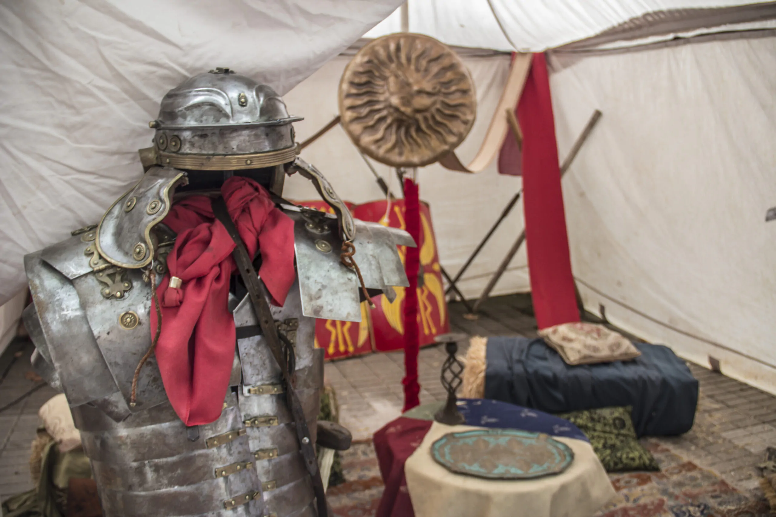 Armadura completa con casco y capa roja en una tienda de campaña decorada con escudos y símbolos romanos