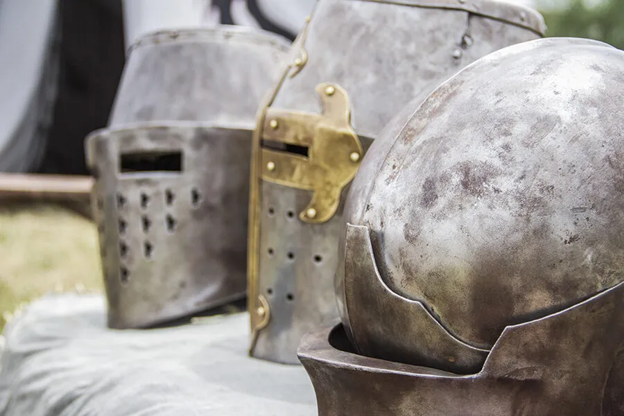 Cascos medievales de metal desgastados en exhibición, mostrando detalles de protección y ornamentación en un evento histórico