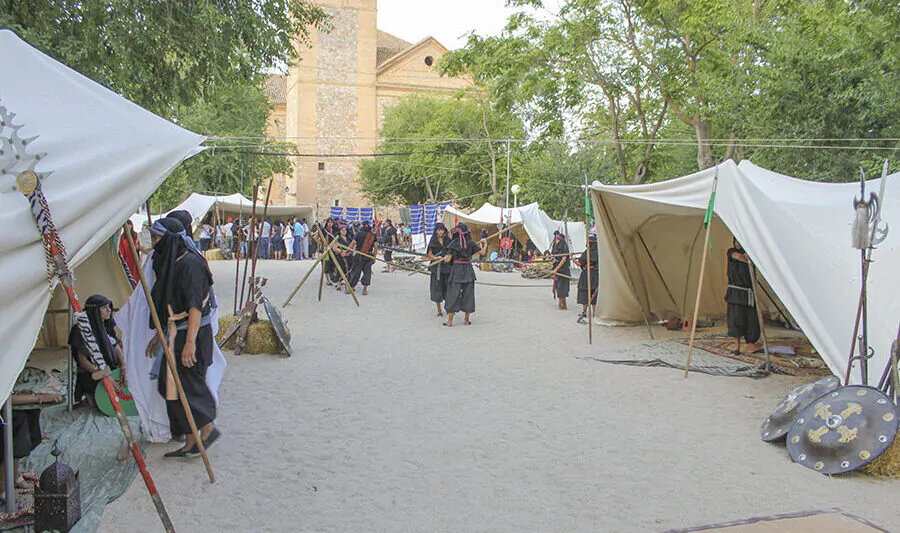 Campamento medieval con tiendas y guerreros entrenando con lanzas, en un evento histórico