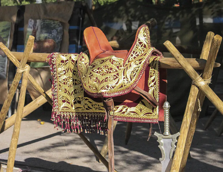 Silla de montar decorada con detalles dorados y espada colocada sobre una estructura de madera