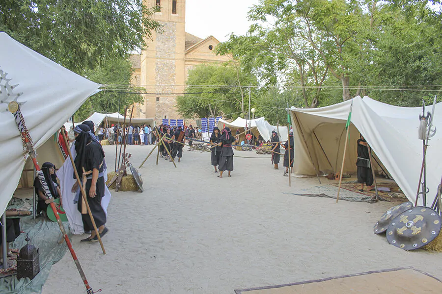 Campamento medieval con tiendas y guerreros entrenando con lanzas