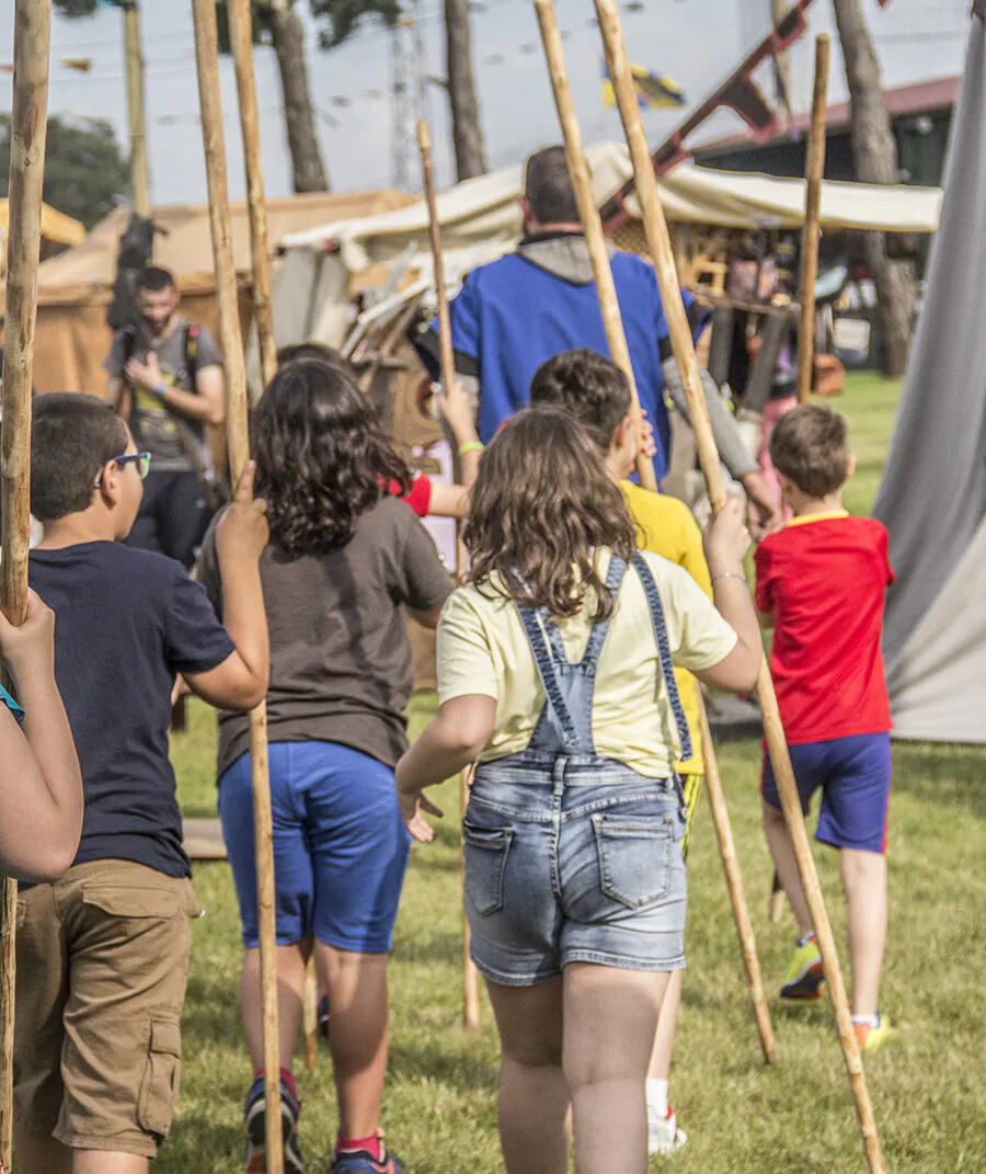 Grupo de niños y niñas participando en una actividad con lanzas de madera en un campamento al aire libre durante un evento educativo