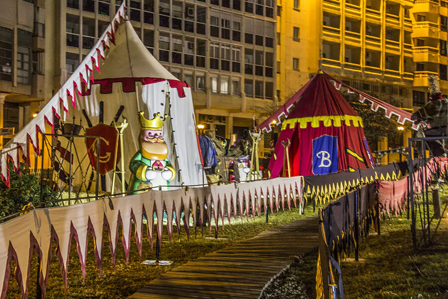 Campamento medieval iluminado con tiendas decoradas y una figura de rey, en una exhibición nocturna temática al aire libre