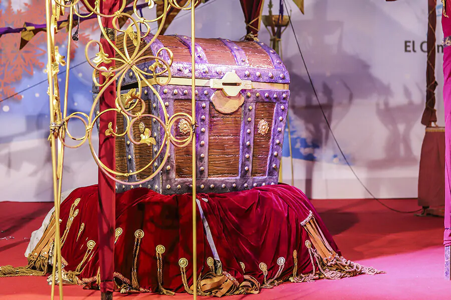 Gran cofre decorado con detalles metálicos sobre un manto rojo de terciopelo en una exhibición temática medieval